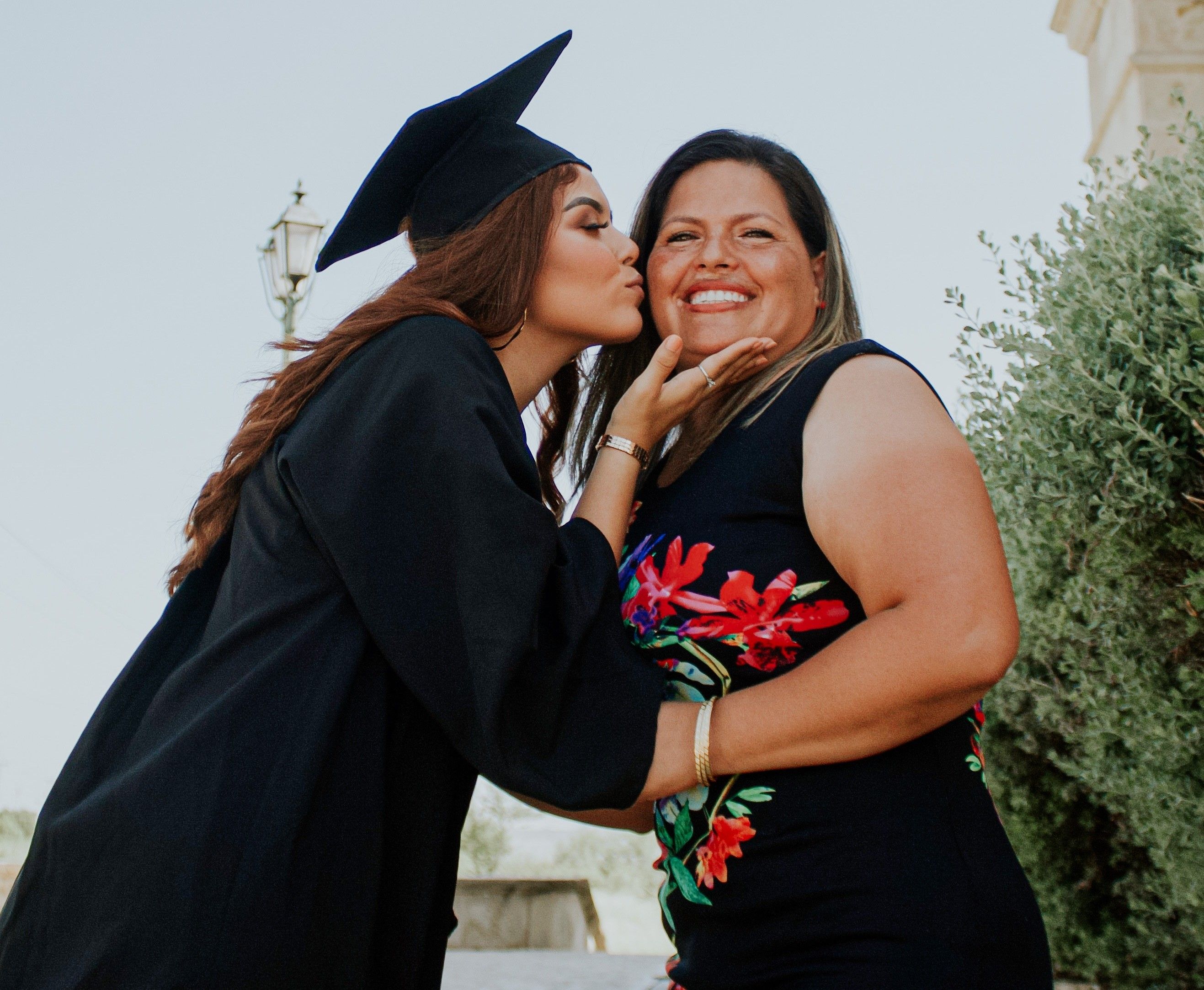 Female graduate kissing smiling mom on cheek