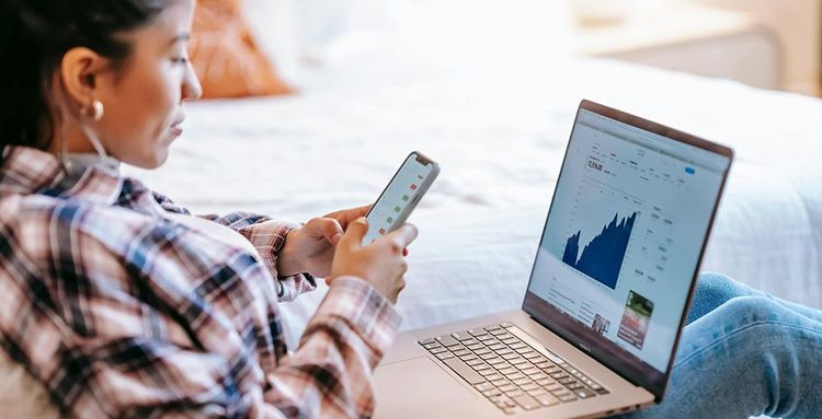 woman reviewing finances on smartphone and laptop