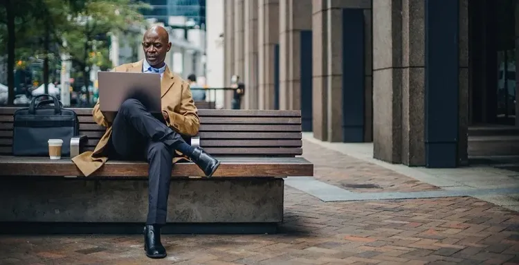 employee sitting on bench working on laptop