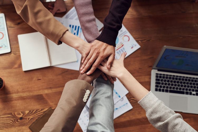 Employees putting hands together while working on financial benefits