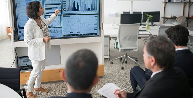 woman in white suit discussing stock market data to her colleagues